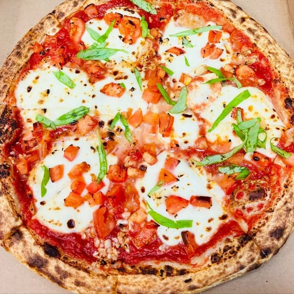 A Doughboys Pizzeria Margherita pizza with fresh mozzarella, diced tomatoes, and basil on a crispy crust.
