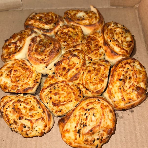 A dozen Doughboys Pizzeria garlic knots, golden brown and sprinkled with herbs, in a cardboard box.