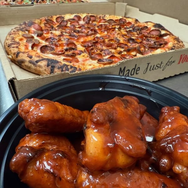 A pepperoni pizza in a box and a black bowl of saucy chicken wings from Doughboys Pizzeria.