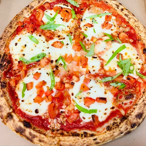 A Doughboys Pizzeria Margherita pizza with fresh mozzarella, diced tomatoes, and basil leaves.