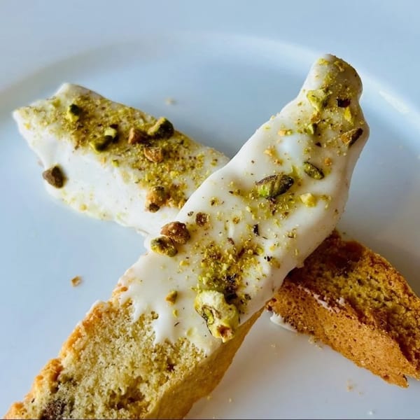 Two biscotti with white icing and chopped pistachios on a white plate at Doughboys Pizzeria.