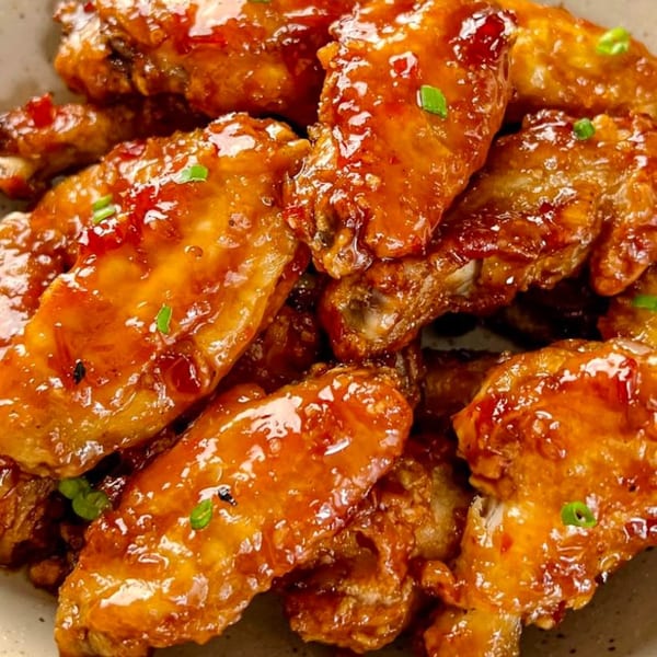 Close-up of Doughboys Pizzeria's glistening, saucy chicken wings, garnished with chopped green onions.
